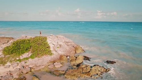 Una mujer explora una gran formación rocosa costera con olas del océano que chocan cerca