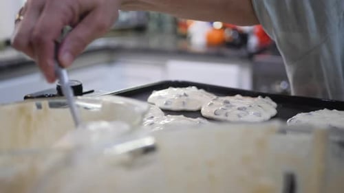 Woman scoops chocolate chip pancake batter onto pan in slow motion