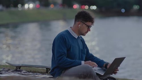 Young Man Using Laptop in City Park by the River