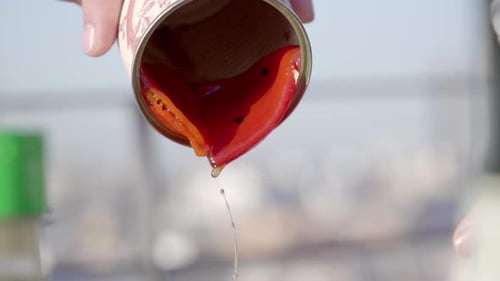 primer plano de una persona vertiendo líquido de una lata, con una salsa roja vibrante o un jugo a raudales.
El