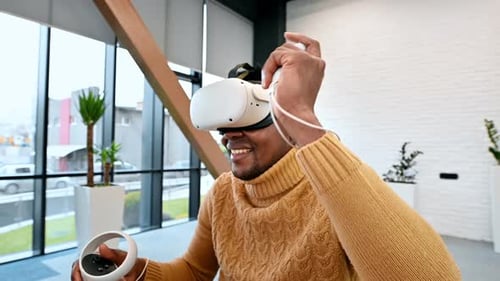 A black man exploring virtual reality using VR glasses and controllers in an office. Slow motion