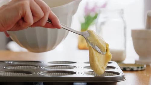 Lächelnde junge Frau kocht zu Hause und verteilt Cupcake-Teig in der Küche