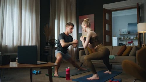 Novio haciendo ejercicio a su novia en casa viendo la lección de entrenamiento en línea en la computadora portátil