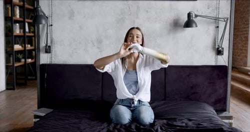 Fille heureuse avec un bras prothétique écoutant de la musique sur le lit à la maison Femme handicapée relaxante et