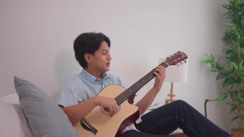 Man Plays Guitar Relaxing on Couch at Home