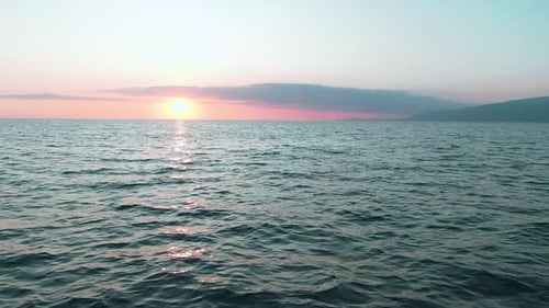 Pink Sunset Over Ocean Calm Water and Distant Mountain Silhouette
