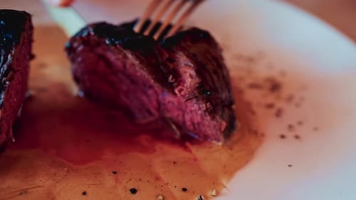 Close up of a knife slicing through a medium rare steak, exposing its tender, juicy interior
