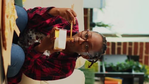 Woman Eating Takeout With Chopsticks Indoors