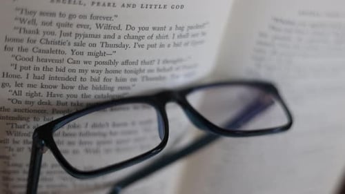Glasses rest on open vintage book pages, text magnified through lenses, symbolic knowledge