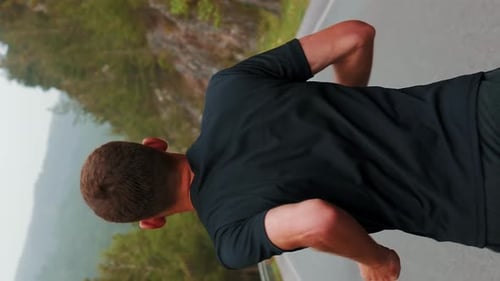Zurück folgen Sie der Aufnahme eines Mannes, der auf einer leeren Straße in den Bergen rennt. Vertikales Video