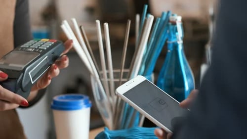 Young woman at restaurant cash desk serving customer paying with nfc phone