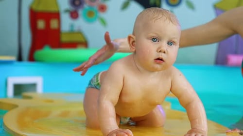 Lovely Caucasian baby boy stands on all four on the floating mat. Little child in the swimming pool.