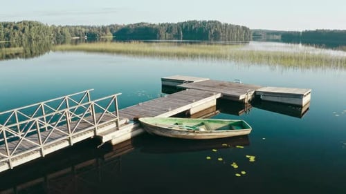 Drone Flies Over Wooden Old Boat Moored at Pier on Large Lake Among Forest