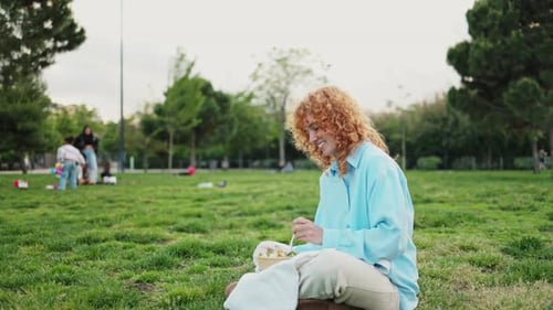Redhead Woman Enjoying a Meal Outdoors in a Park