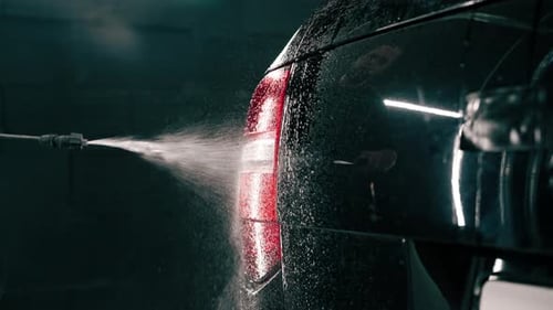 A male car wash employee applies car wash detergent to a black luxury car using spray gun in the car