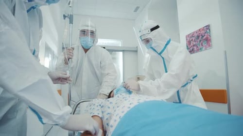 Doctors in PPE tending patient on gurney in hospital