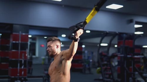 Muscular Man Training with Suspension Straps in Gym