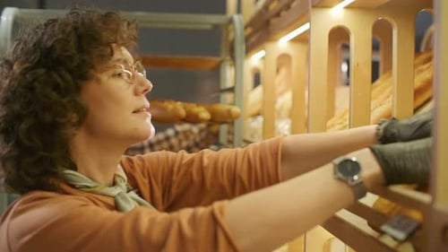 Female Bakery Worker Arranging Fresh Baguettes on Shelf for Sale
