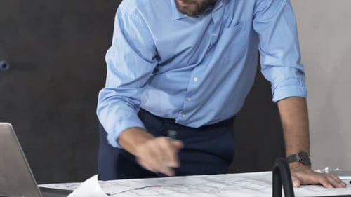 Professional Man Reviews Blueprints in an Office Setting