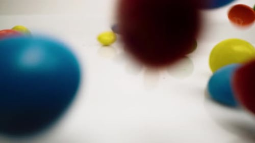Bunte Schokoladenbonbons von M und M springen in Zeitlupe auf einer weißen reflektierenden Platte herum