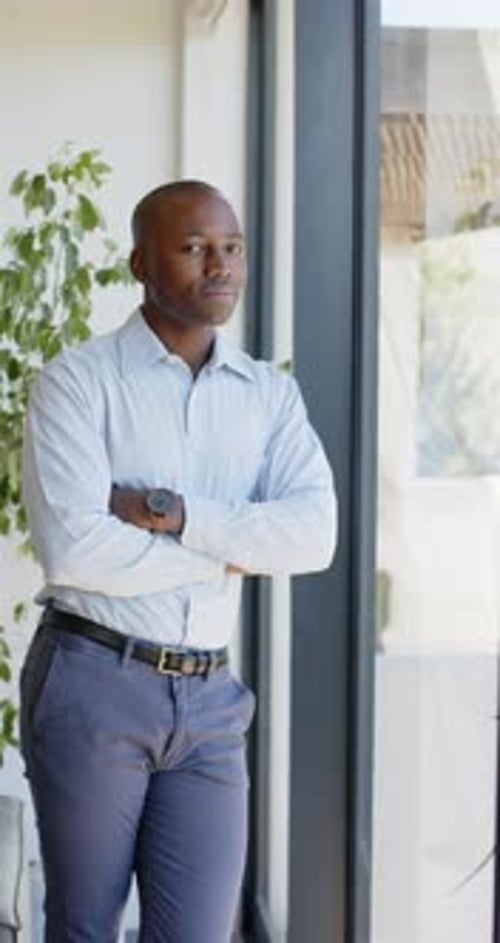 Vertical video: Confident businessman standing with arms crossed near window in office