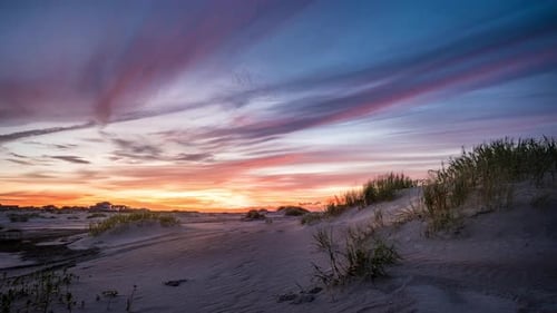 Time lapse of sand dunes, a beach, a few cars, clouds and a colorful sunrise. Dawn turns to a bright