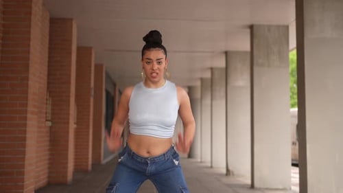 A Woman in a Blue Tank Top and Blue Jeans is Dancing in Front of a Building
