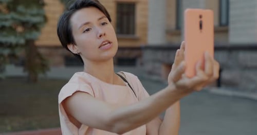 Joyful Young Lady Making Online Video Call with Smartphone Speaking Sending Air Kiss in City