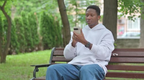 Young Adult Using Smartphone on a Bench in Park