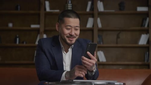 Asian Businessman Greeting and Talking on a Video Conference Call Using Smart Phone in Loft Office