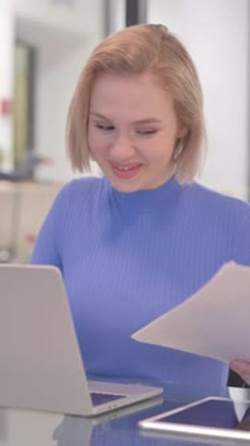 Woman Working on Laptop and Holding Documents