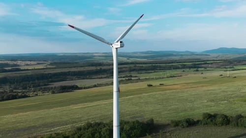 Aerial panoramic shot around single wind turbine generator in grass field