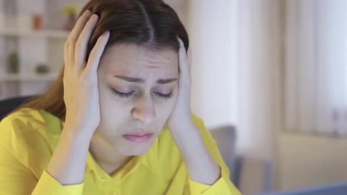 Sad and worried young woman looking at laptop at home and feeling frustrated.