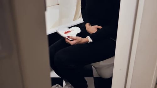 Woman Holding Bloody Sanitary Pad During Painful Menstruation In Bathroom