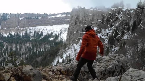 Hiker in winter clothes walk to cliff edge, raise arms. Overlook winter landscape. Success winning c