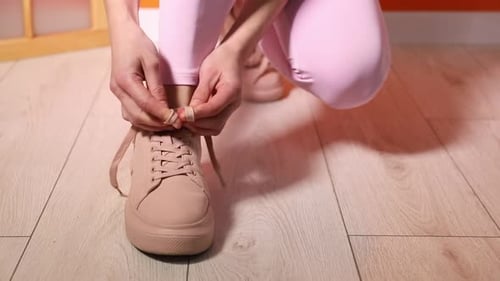 Woman tying shoelace of beige sneaker indoors, closeup