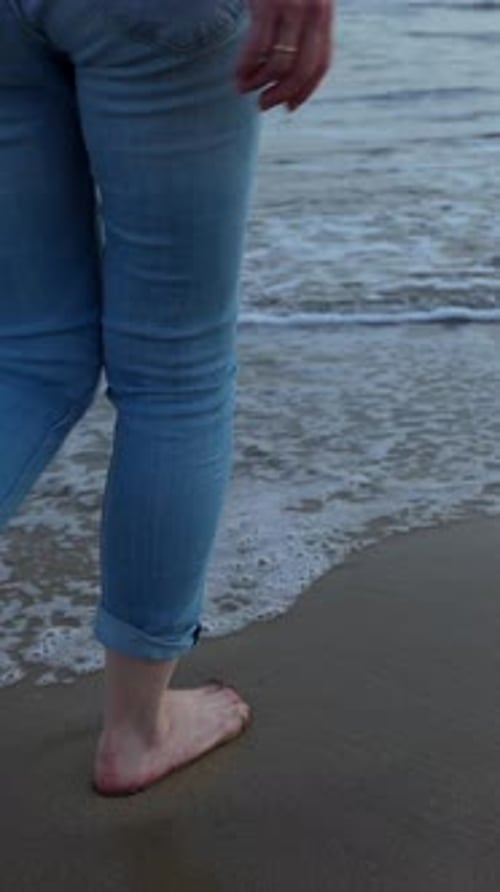 Woman's bare feet walking at the water's edge on a sandy beach at sunset