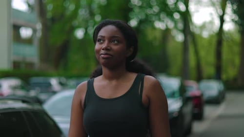 African American woman walking forward along residential street with soft smile and daydreaming