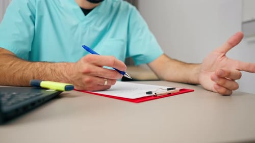 Close-up shot of a male doctor's hand with ring on his finger filling out patient's medical history