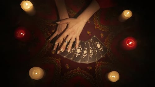 Ansicht von oben auf einen Fan von Tarotkarten, der auf dem Tisch liegt, weibliche Hände bewegen sich langsam über die Karten und