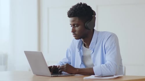 Young Man Typing on Laptop Wearing Headphones