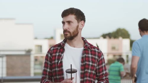 Bearded Man Holds Drink on Rooftop with Friends
