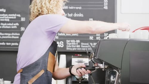 Caucasian male barista wearing apron preparing coffee with coffee machine in cafe