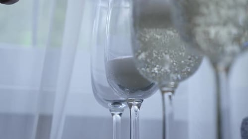 44s. Pouring white, sparkling champagne into glasses. Shot in a dark key.