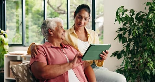 Smiling Woman and Senior Woman Use Tablet Together Indoors
