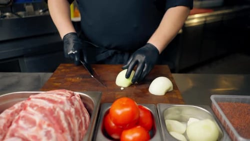 Close Up in a Professional Kitchen a Chef in a Black Uniform Chops Onions on a Board