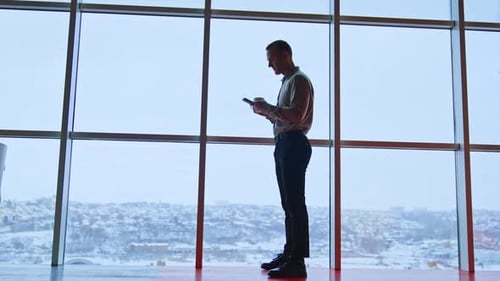 Office employee at the window with phone and white cup.