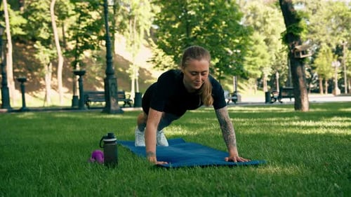 portrait of a young satisfied sports girl doing push-ups outdoors while exercising in the park