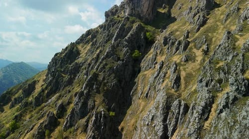Aerial scenic view of a rocky mountain peak with lush greenery under a clear blue sky, perfect for o