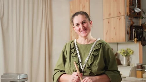 Cheerful Cook in Green Gown Holding Spatula and Smiling in Kitchen Scene